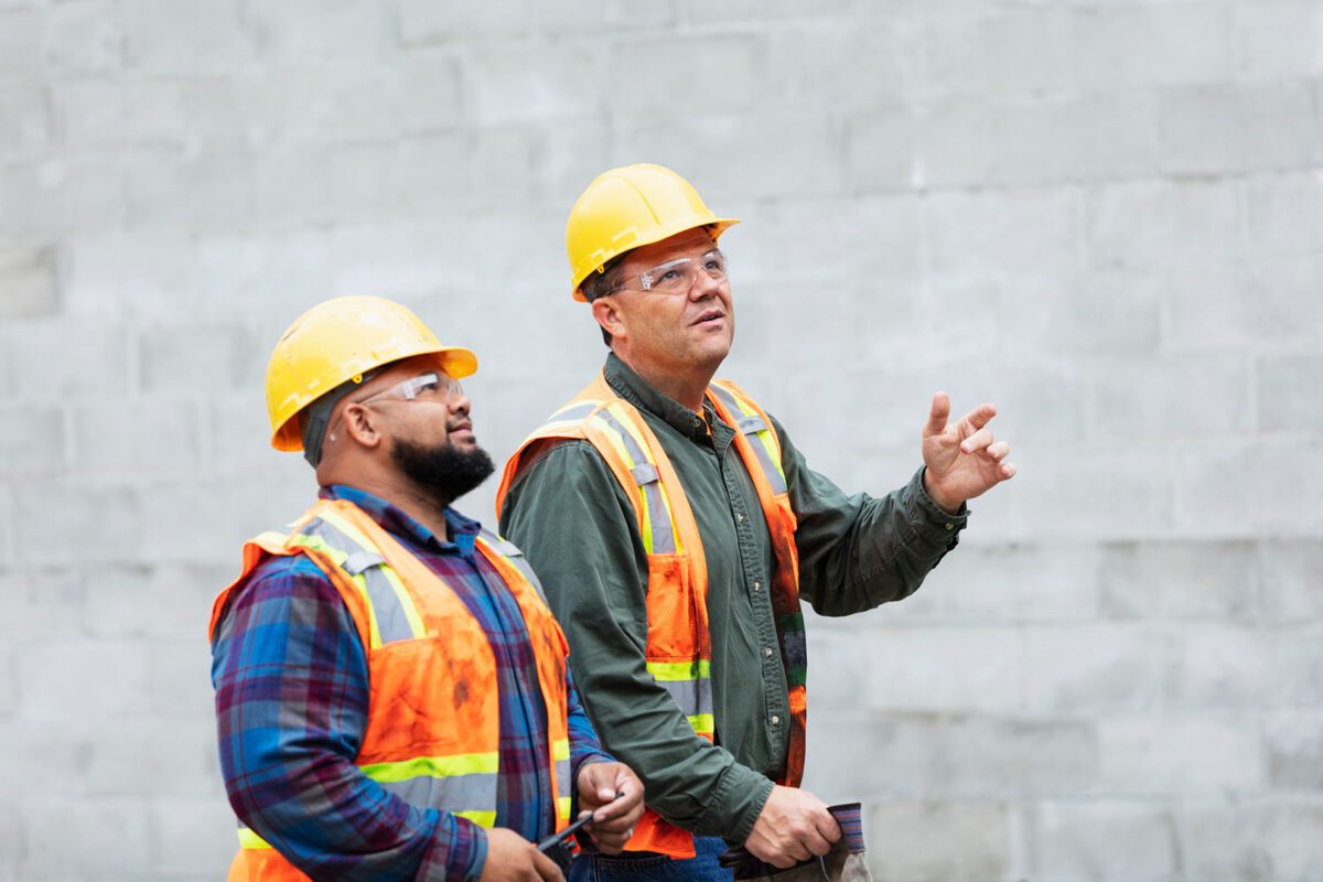 2 men in custruction vests and hard hats looking upward