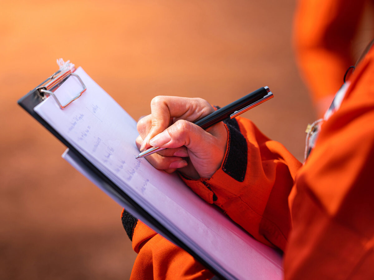 A female construction worker holding a pen and writing a list on a clipboard.